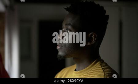 Pensive black African man standing by window, close-up face thinking Stock Photo