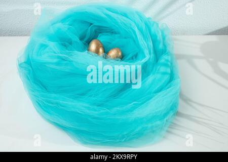 Golden eggs in a blue fabric nest, on white background Stock Photo
