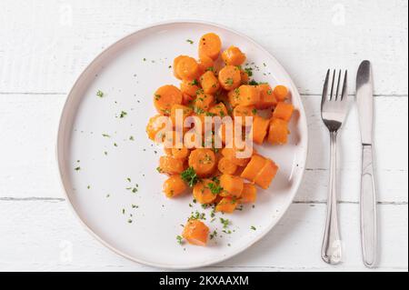 Buttered carrots with parsley on a plate for side dish. Served isolated on white wooden background. Flat lay Stock Photo
