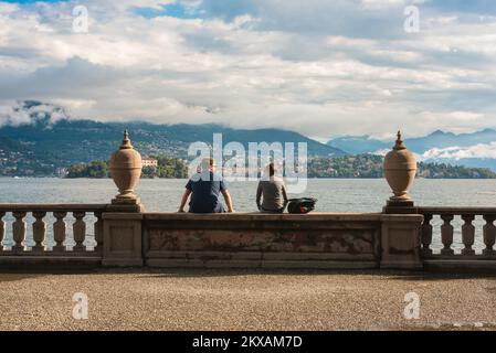 Travel couple, rear view of a young man and woman sitting together in the grounds of Palazzo Borromeo, Isola Bella, Lake Maggiore, Italy, Europe Stock Photo