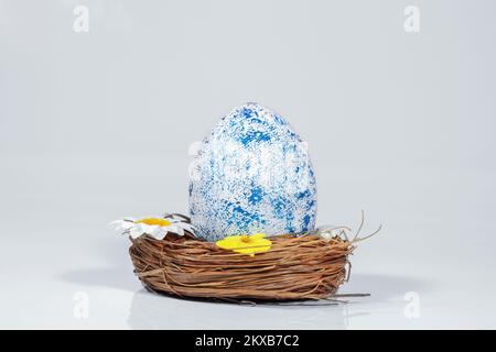 Easter card. Toned blue chicken egg in a nest with flowers, isolated on gray background. Easter concept. Copy space Stock Photo