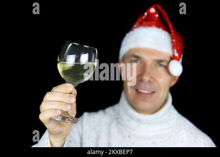 Wine glass in hand of happy man in Santa Claus hat on black background. Christmas celebration, New Year party Stock Photo