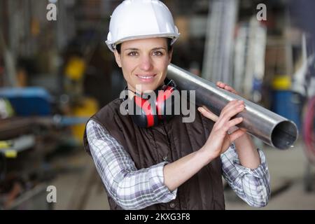 female engineer carrying pipes while looking at camera Stock Photo