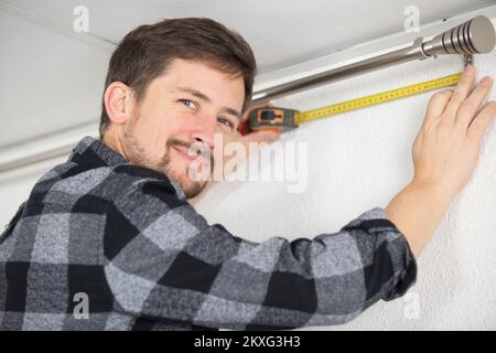 man measuring under a curtain rail Stock Photo