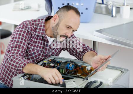 mature serviceman working on appliance and holding tablet Stock Photo