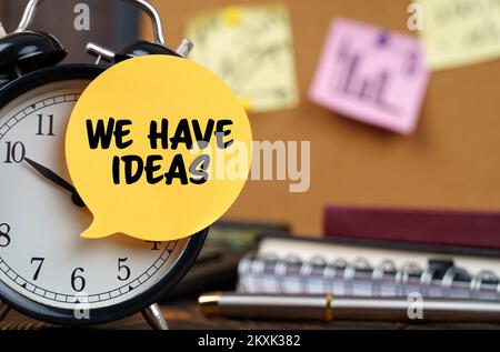 Business concept. The alarm clocks have a sticker with the inscription - We Have Ideas. There are office items in the background in a blurry backgroun Stock Photo