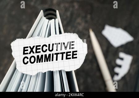 On the table is a notebook on which lies a piece of torn paper with the inscription - Executive Committee. The pen lies outside the sharpness zone. Stock Photo