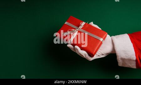 Cropped Santa's Hand Giving Gifts Against Green Background Stock Photo