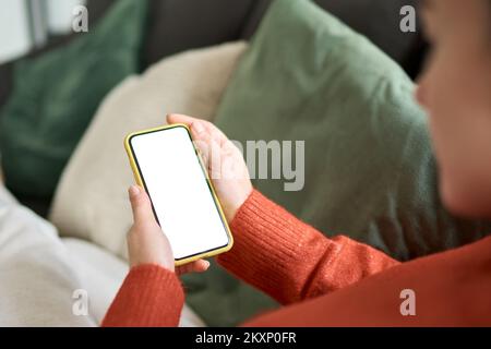 Woman holding mobile phone white mockup screen relaxing at home, over shoulder. Stock Photo