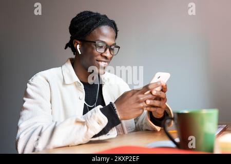 Happy black guy freelancer reading text message on smartphone while working remotely from home Stock Photo