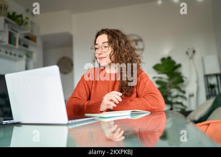 Young female student using laptop watching online webinar writing at home. Stock Photo