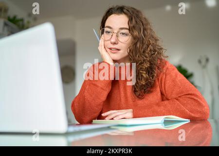 Young woman student using laptop watching online webinar writing at home. Stock Photo