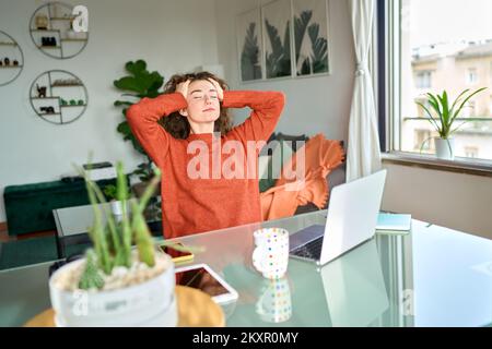 Young woman taking break from remote computer work at home to relax . Stock Photo
