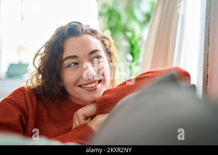 Young happy dreamy woman relaxing sitting on couch at home, dreaming. Stock Photo