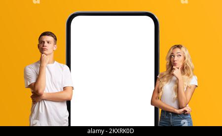 Thoughtful Young Man And Woman Standing Near Big Blank Smartphone Stock Photo