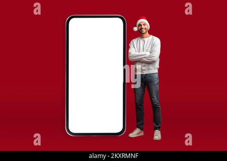 Online Offer. Handsome Arab Man In Santa Hat Posing Near Blank Smartphone Stock Photo