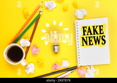 Business and technology concept. On a yellow background, a cup of coffee, a light bulb, pencils, a notebook with the inscription - FAKE NEWS Stock Photo