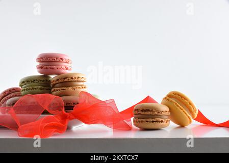 Presentation of ssortment of french macaroons of various flavors in white plate on table with red tie and white isolated background. Front view. Stock Photo