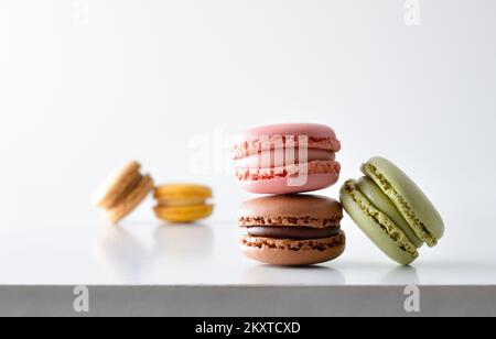 Detail of French macaroons of various flavors reflected on white table and white isolated background. Front view. Stock Photo