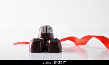 Stacked chocolate bonbons with red bow on white table isolated with white background. Front view. Stock Photo