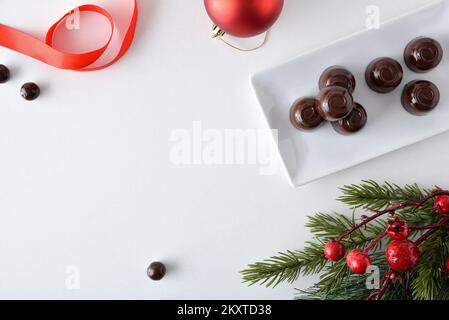 Chocolate candies on a rectangular plate on a white table with Christmas decorations. Top view. Stock Photo