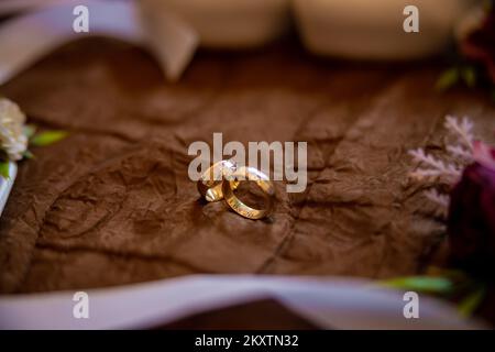 Two golden wedding rings on a brown bed cover with flowers around them. Bride and groom rings. High quality photo Stock Photo