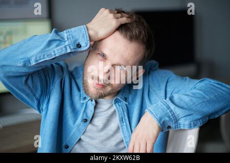 Young attractive freelancer guy at home office correcting his haircut looking at camera. Cute bearded caucasian male software engineer sitting at working place. High quality image Stock Photo
