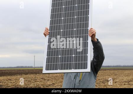 A man holds a solar panel in his hands against a cloudy sky. Stock Photo