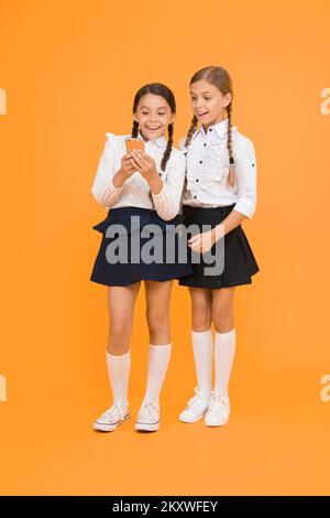 Internet is wonderful resource but access to it has hazards for kids. Girls school uniform using smartphone. Schoolgirls use mobile phone or Stock Photo