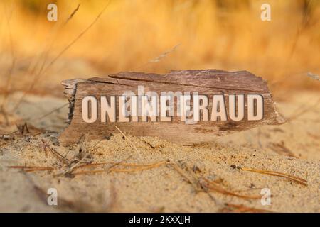 Internet and computers concept. On the sand against a background of yellow grass, a signboard with the inscription - ONLINE FRAUD Stock Photo
