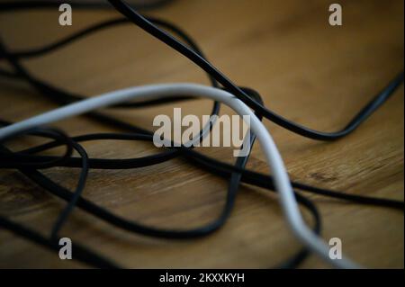 Cable chaos clutter from multiple electric wire extension cords and multi-contact plugs on wooden floor or table background Stock Photo