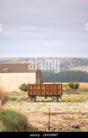 Rural image of a tractor trailer used in agriculture parked in a farm field near a shed Stock Photo