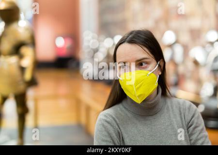 Female museum visitor in protective mask examining ancient armor Stock Photo