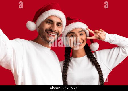 Happy Young Middle Eastern Couple In Santa Hats Taking Selfie Together Stock Photo