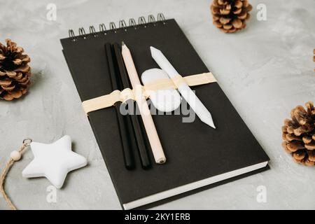 Sketchbook or notebook, pencils, eraser, pine cones, star on desk workspace, gray background. Christmas and New Year gifts for artist or children and lifestyle concept. Flat lay, top view, copy space Stock Photo