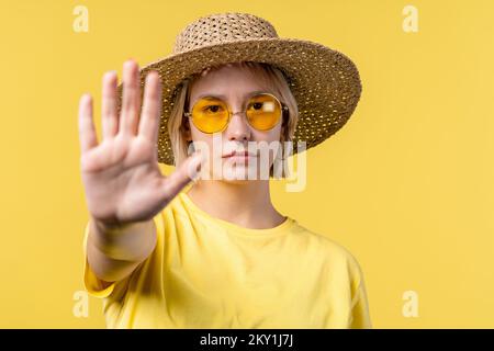 Uninterested woman disapproving with NO hand sign gesture. Denying, rejecting, disagree. Portrait of young lady on yellow background, timeout concept. Stock Photo