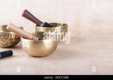 Tibetan singing bowls with sticks used during mantra meditations on beige stone background, copy space. Sound healing music instruments for meditation Stock Photo