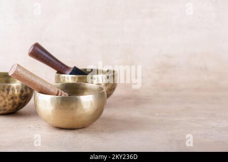 Tibetan singing bowls with sticks used during mantra meditations on beige stone background, copy space. Sound healing music instruments for meditation Stock Photo