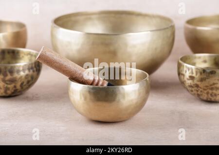 Tibetan singing bowls with sticks used during mantra meditations on beige stone background, close up. Sound healing music instruments for meditation, Stock Photo