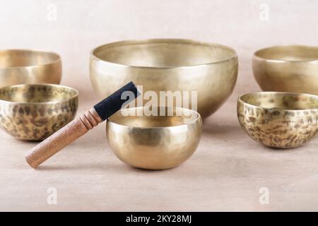 Tibetan singing bowls with sticks used during mantra meditations on beige stone background, close up. Sound healing music instruments for meditation, Stock Photo