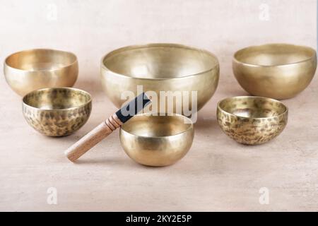 Tibetan singing bowls with sticks used during mantra meditations on beige stone background, close up. Sound healing music instruments for meditation, Stock Photo