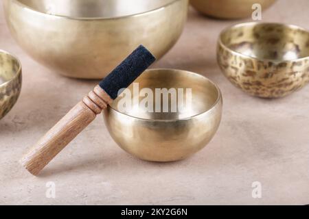 Tibetan singing bowls with sticks used during mantra meditations on beige stone background, close up. Sound healing music instruments for meditation, Stock Photo