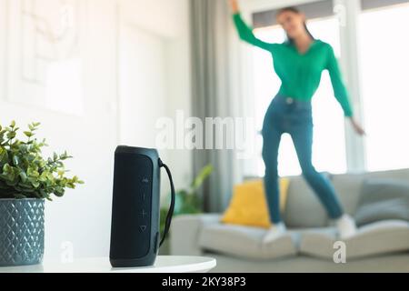 Unrecognizable woman listening to music via music speaker and dancing on sofa, enjoying great playlist, selective focus Stock Photo
