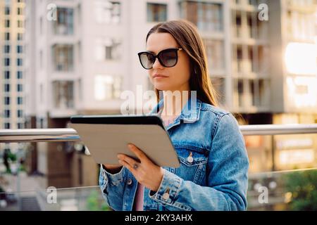 Young business woman millennials in glasses walking Financial District city uses digital tablet in Social networks, Connection, Data, Digital display Stock Photo