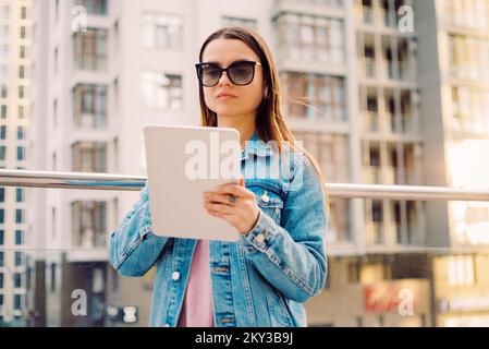 Young business woman millennials in glasses walking Financial District city uses digital tablet in Social networks, Connection, Data, Digital display Stock Photo