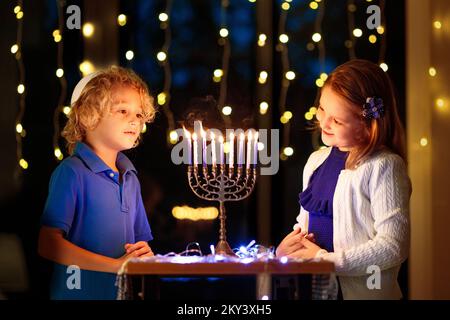 Kids celebrating Hanukkah. Jewish festival of lights. Children lighting candles on traditional menorah. Boy in kippah with dreidel Stock Photo