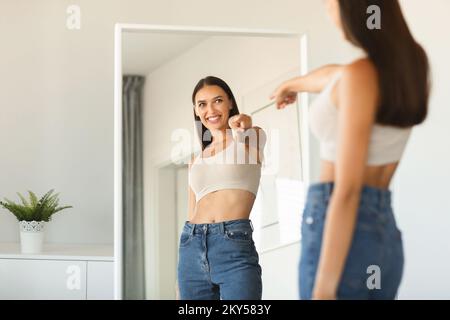 I choose myself. Playful young lady pointing finger at her reflection in mirror enjoying successful slimming, free space Stock Photo