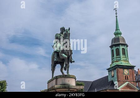 Copenhagen, Denmark - July 24, 2022: King Christian X equestrian greenish bronze statue on beige stone pedestal and spire of Garnison Church at Saint Stock Photo
