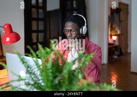 Young African man student wearing headphones watching webinar on laptop while studying online Stock Photo