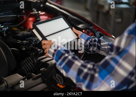 Caucasian female auto mechanic changes the engine air filter in the car. Stock Photo